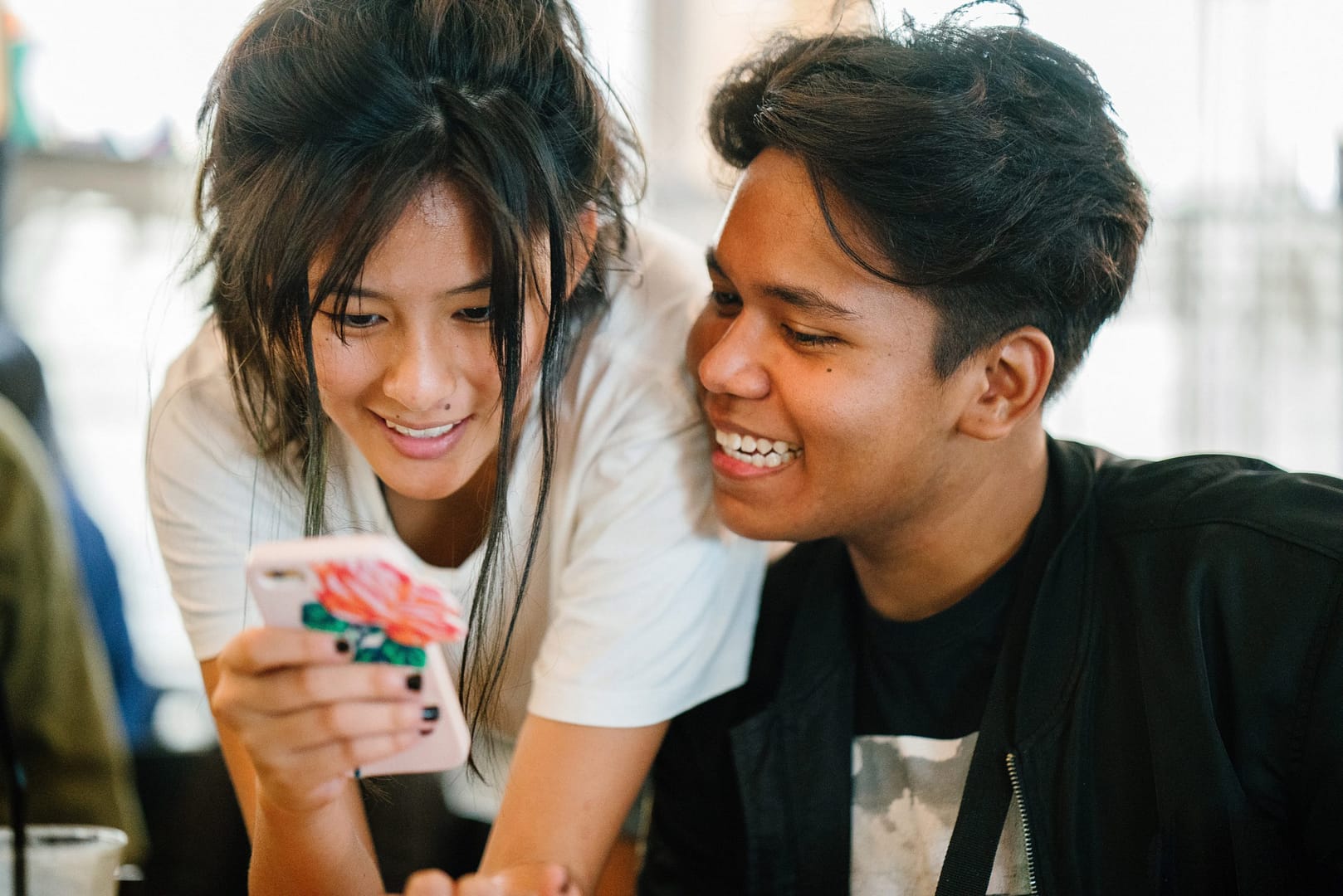 Dois estudantes adolescentes rindo juntos olhando para a tela do celular